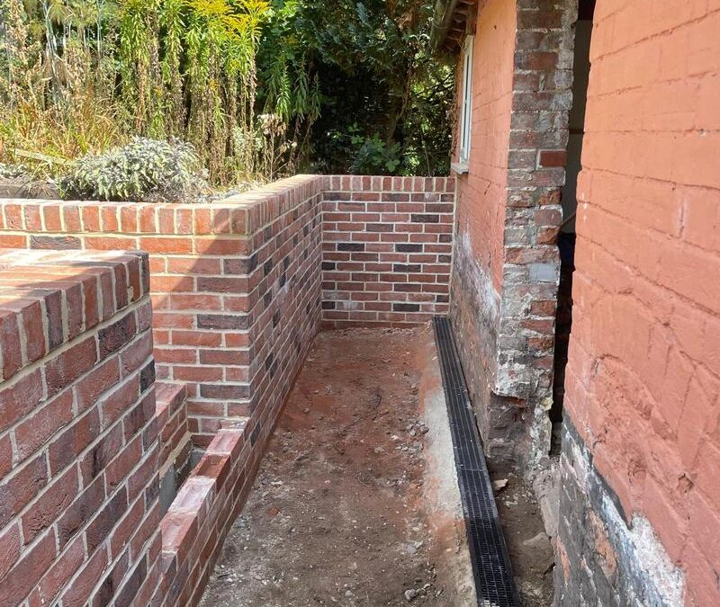 Narrow passageway between brick walls with drainage channel fitted along house foundation